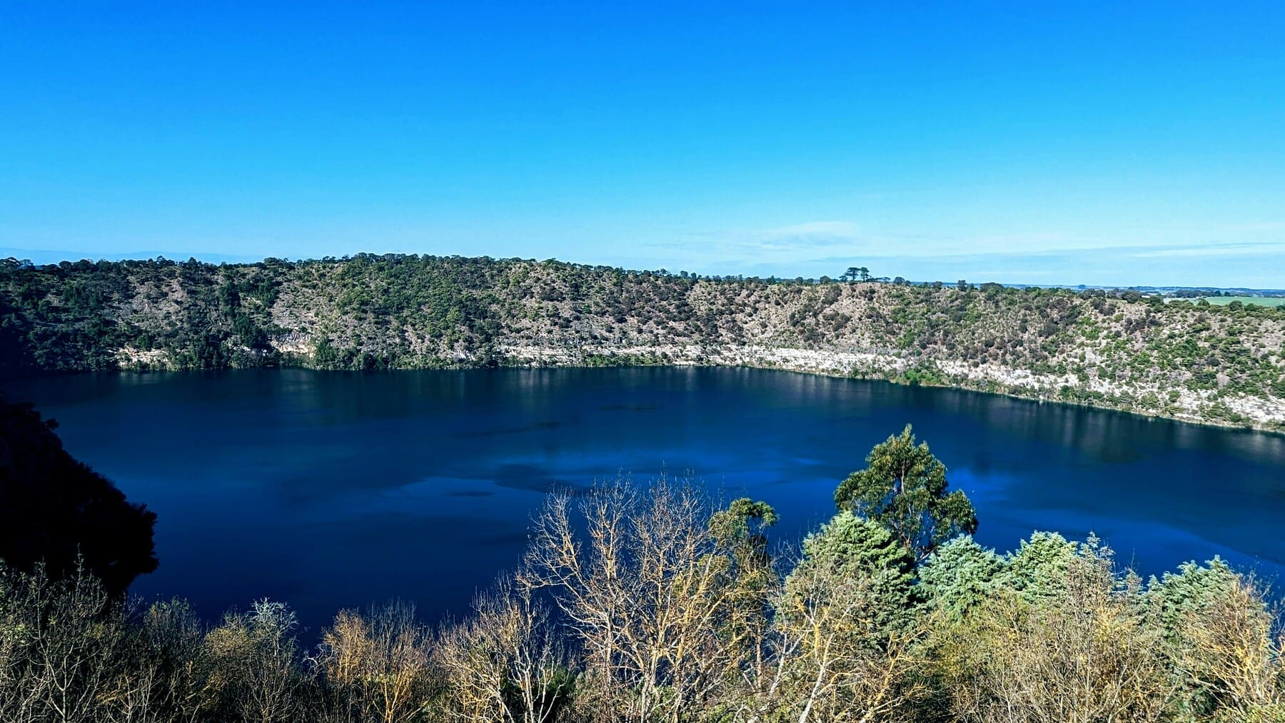 Blue Lake in Mount Gambier surrounded by greenery under clear sky, South Australia.